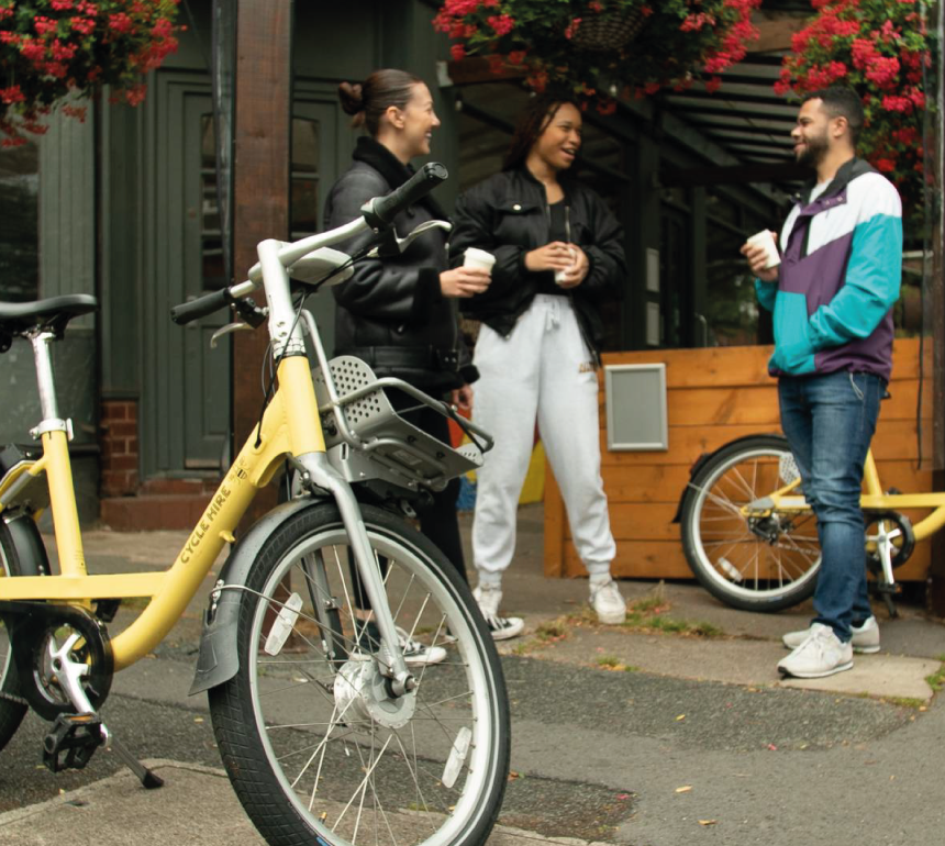 Group of people chatting outside a cafe with cycle hire bikes in the foreground