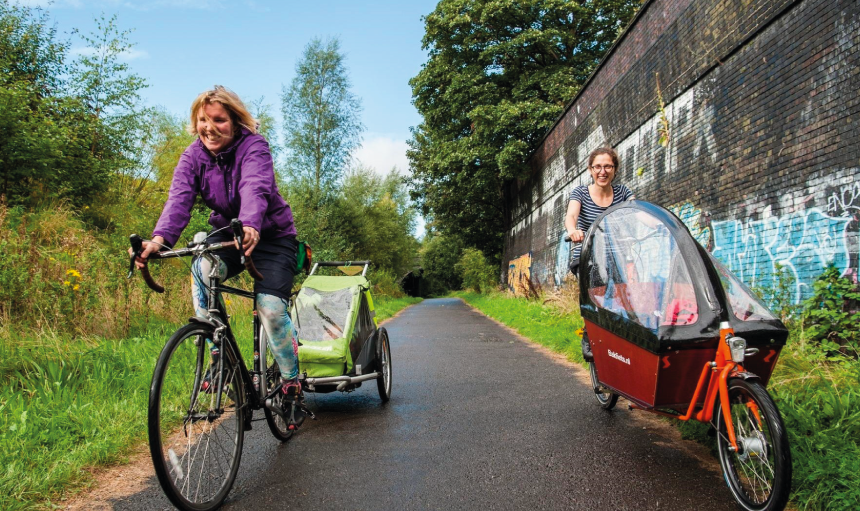 Two women on bikes with child trailers on a tarmacked cycle way