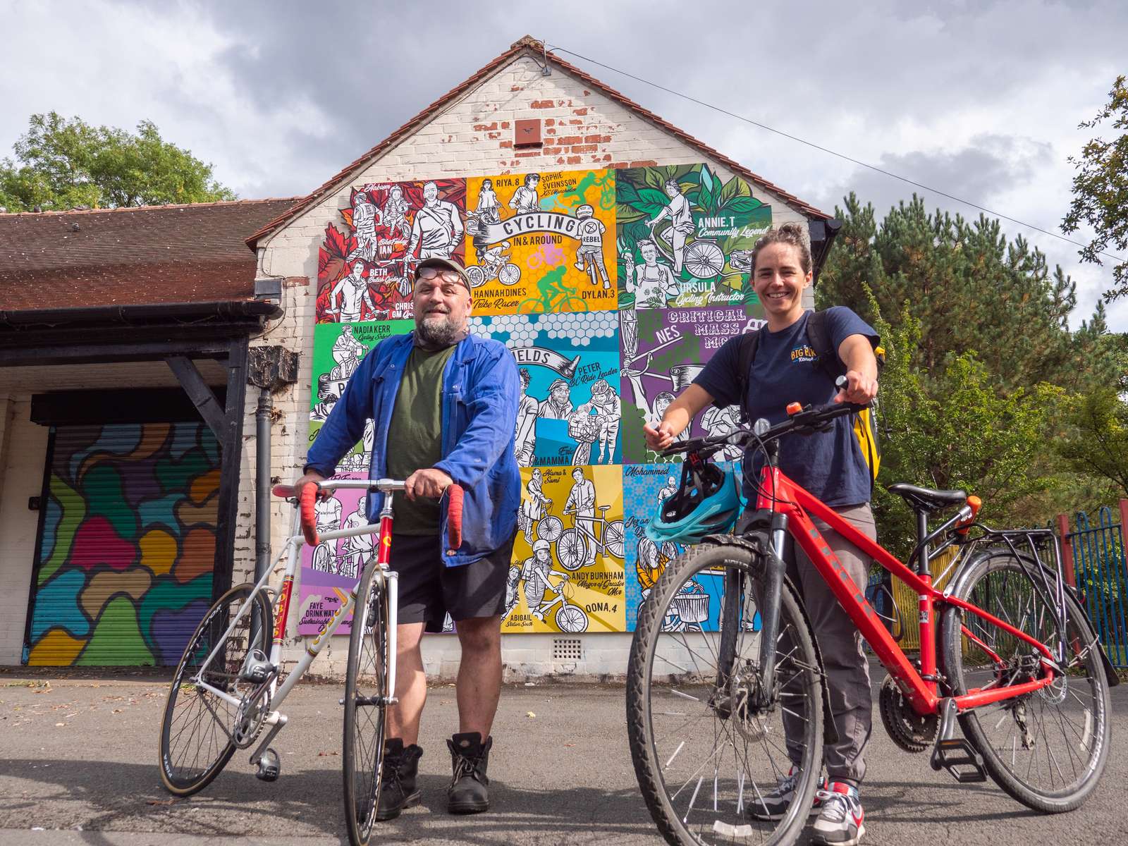 Two people holding bikes in front of a community cycling hub building