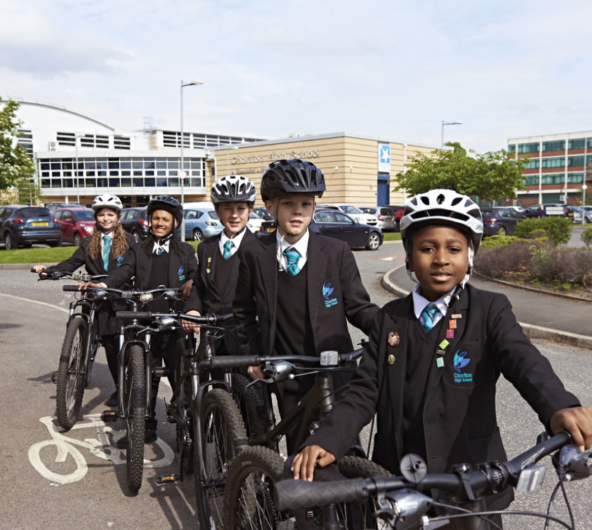 A line of school children standing with bikes in front of a school building