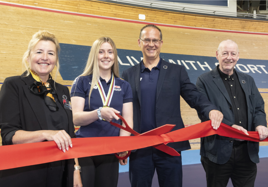 Group of people cutting a red ribbon with an indoor cycling track in the background
