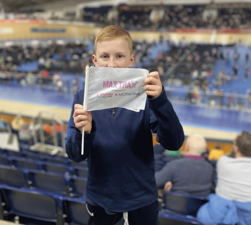 Child at National Track Championships holding flag labelled Max Trax