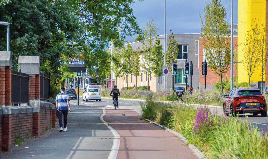 Man walking on Path, person cycling in cycle lane and car driving on road in Manchester